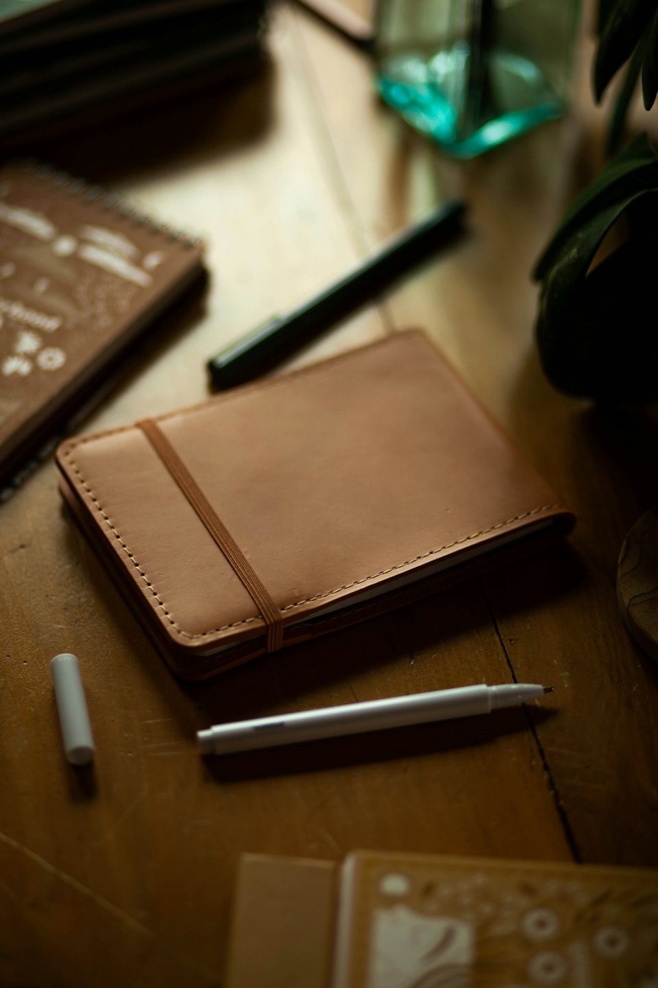 Brown leather notebook with pens on a wooden desk.