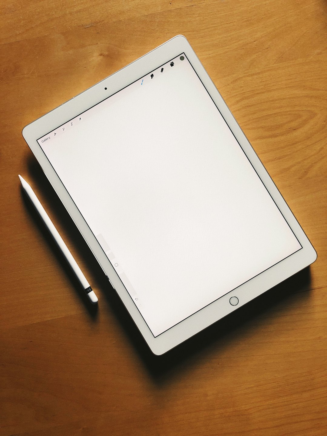 A white digital tablet and stylus rest on a wooden desk.